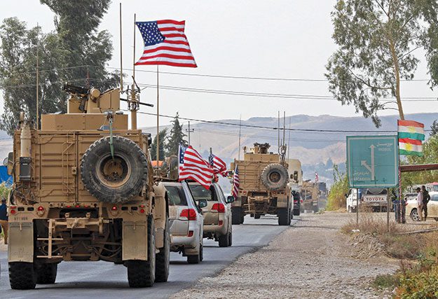 Convoy of military vehicles with American flags driving down a road.