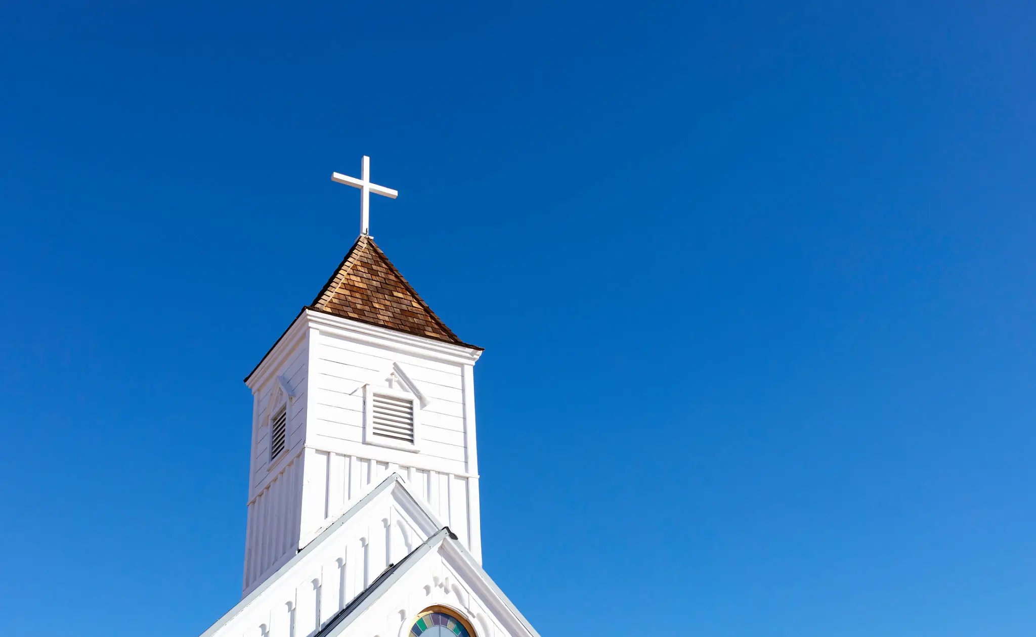 White church steeple with a cross under a clear blue sky.