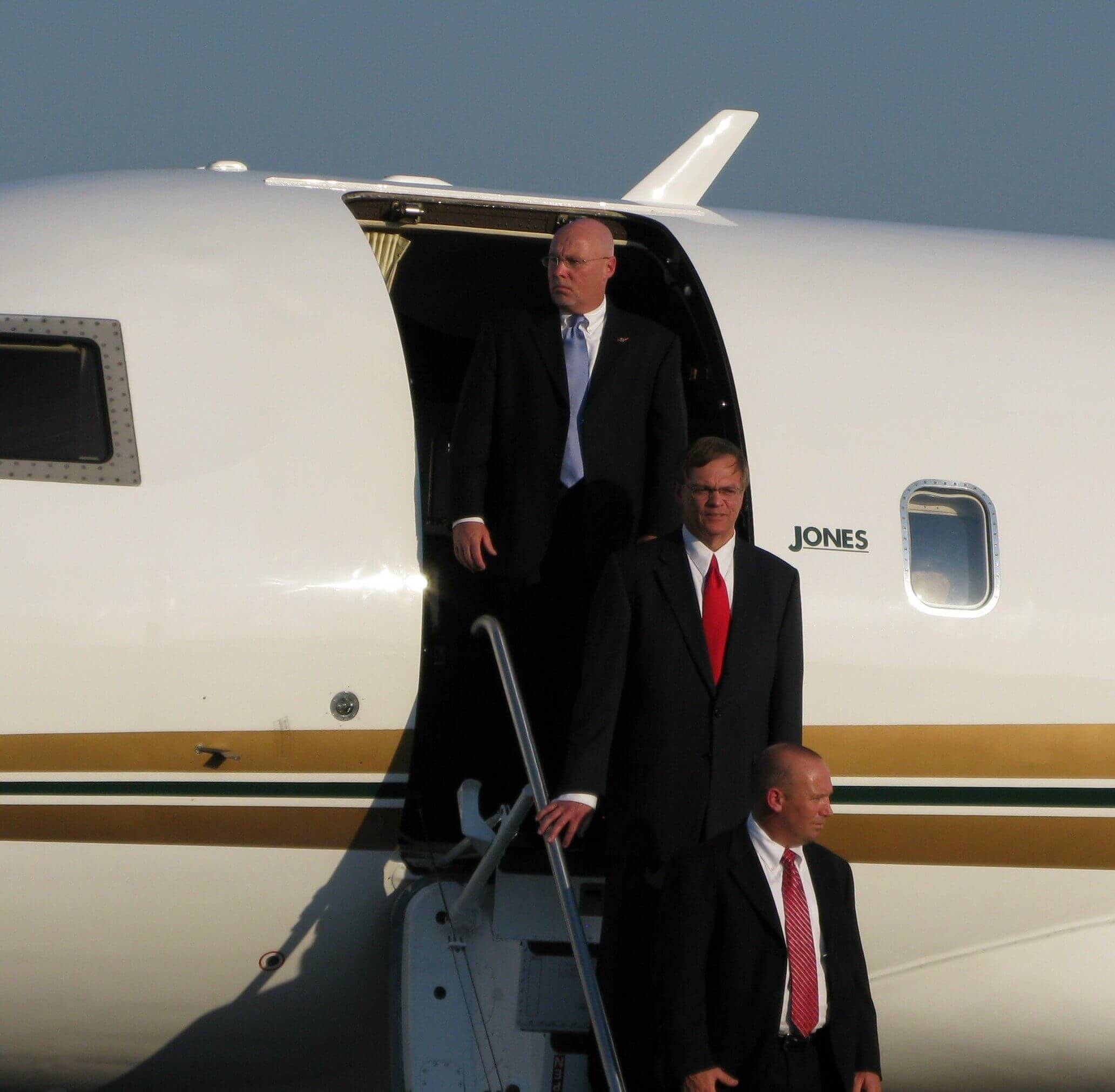 Three men in suits descending stairs from a private jet.
