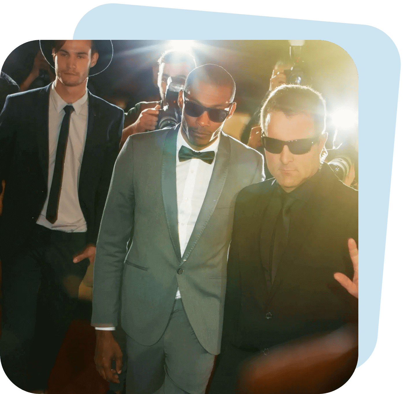 Three men dressed stylishly, two wearing sunglasses, posing confidently in a warm, glowing light.