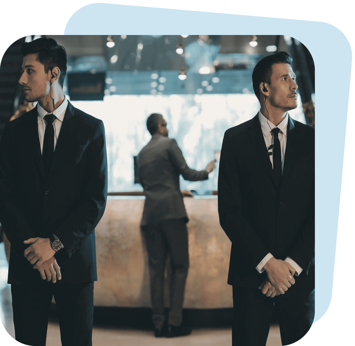 Two suited security guards standing vigilant with a person in the background.