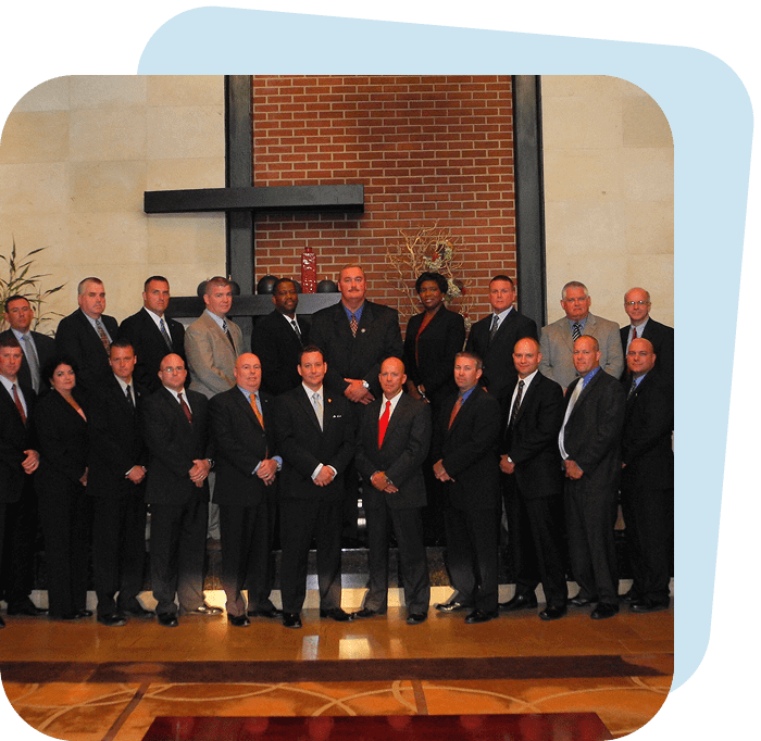 A large group of men in formal suits posing indoors.