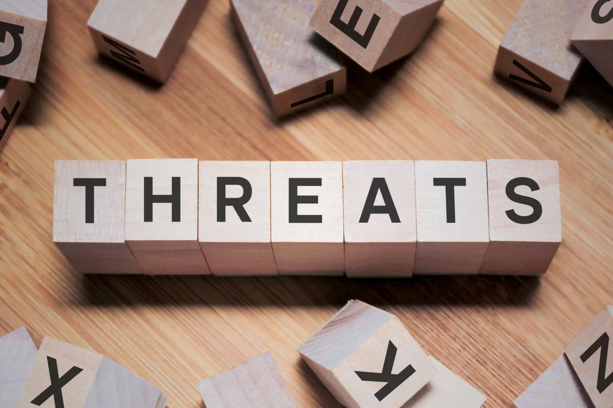 Wooden blocks spelling 'THREATS' on a table with scattered letters.