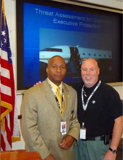 Two men posing together at a professional event with an American flag in the background.